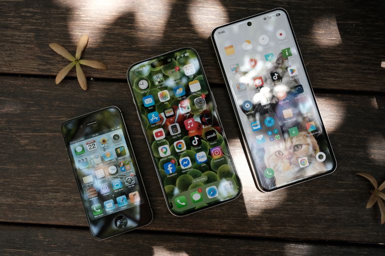 A collection of smartphones showing different app icons, placed on a wooden surface in natural light.
