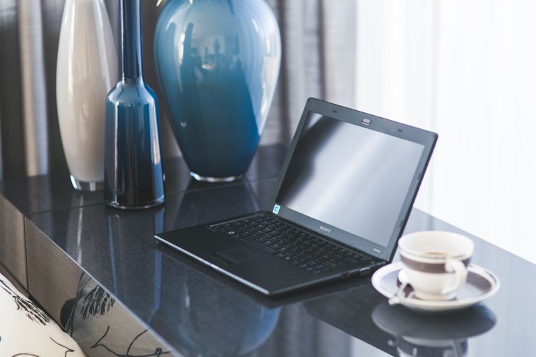 A sleek home office setup featuring a laptop, coffee cup, and decorative vases on a glass table.
